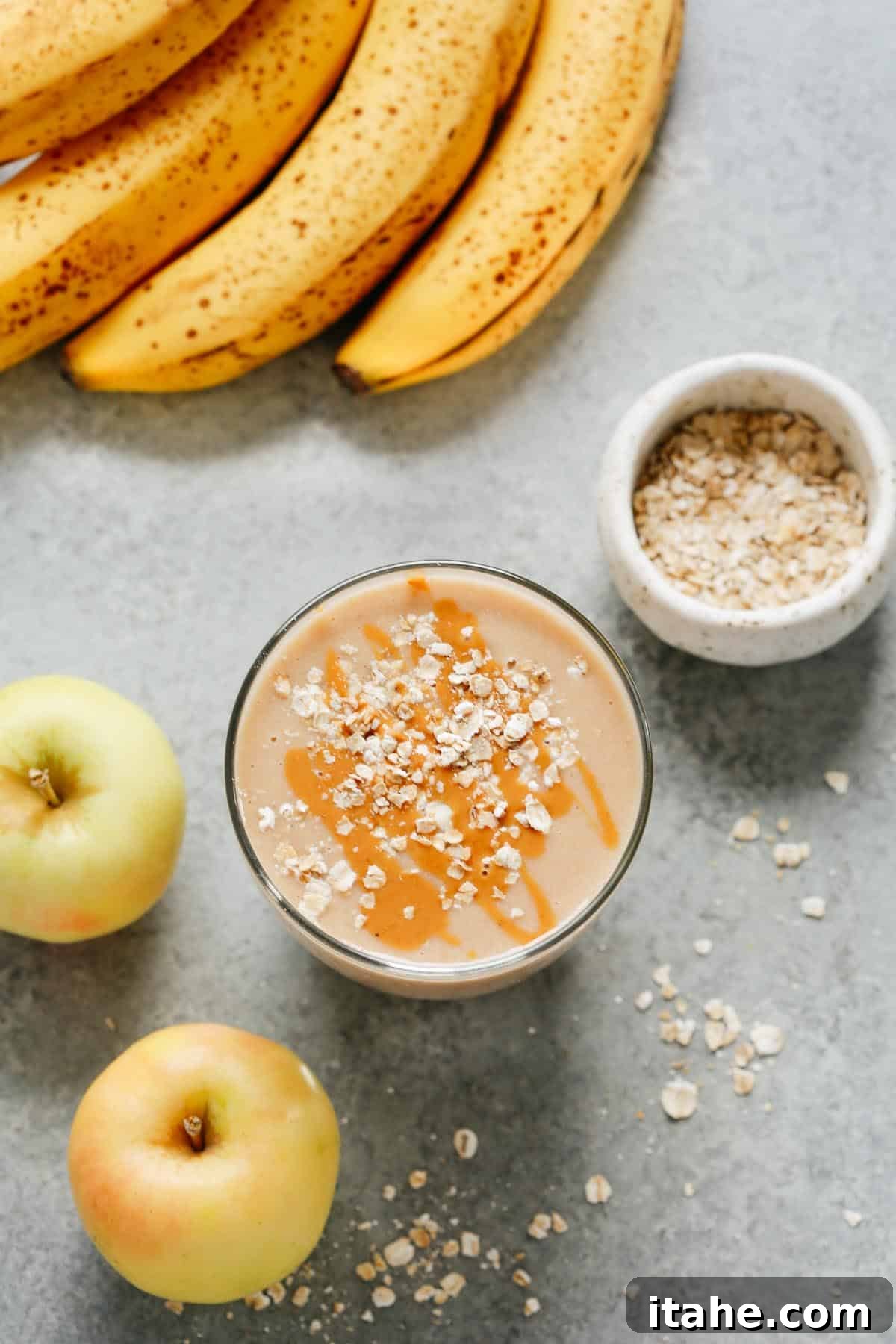 Crisp Apple Blend 4 A beautifully composed shot featuring a cup of apple smoothie garnished with oats, surrounded by fresh bananas, whole apples, and dry oats, highlighting the fresh ingredients used.