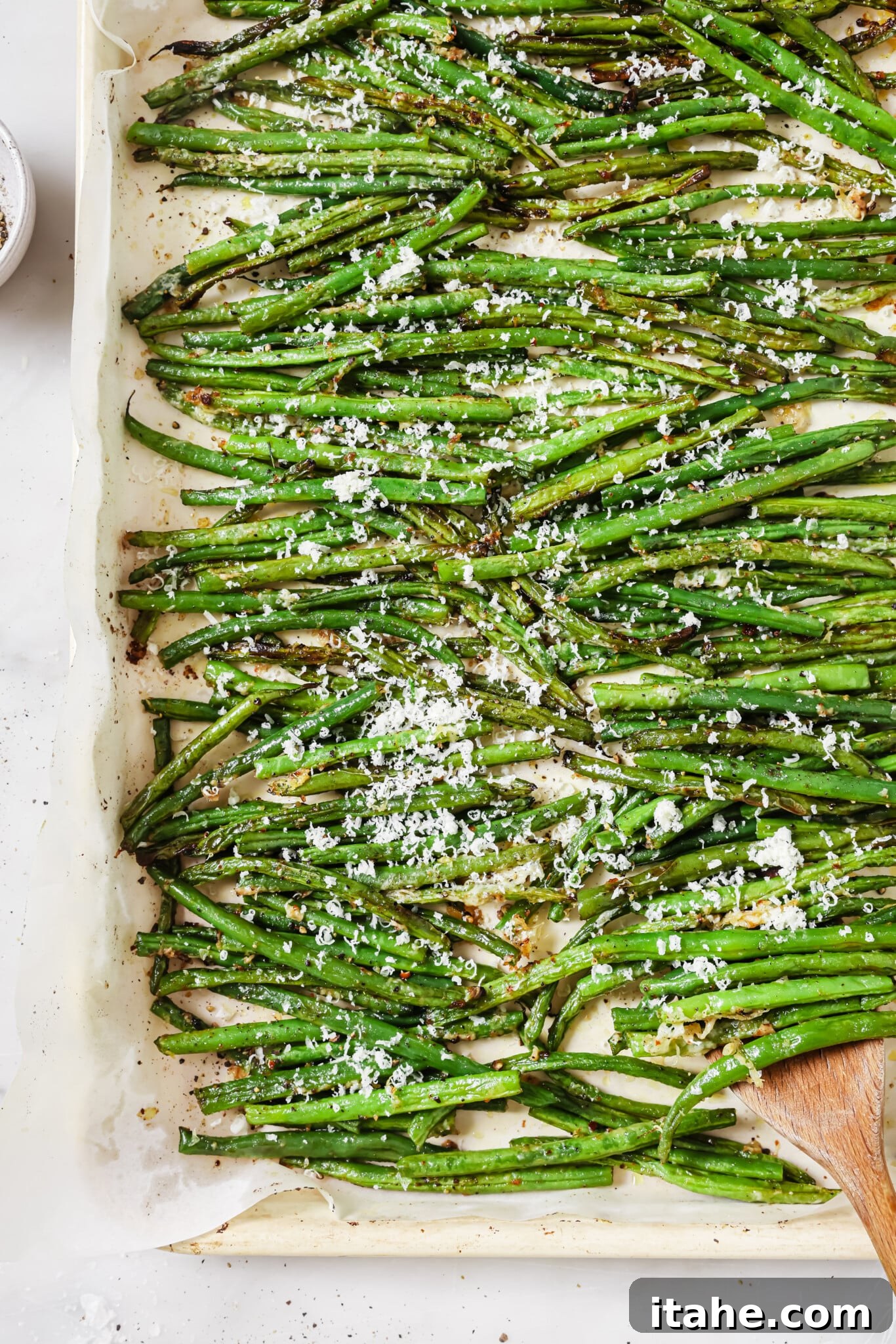 Close up of a baking sheet of parmesan green beans, garnished with fresh parsley.