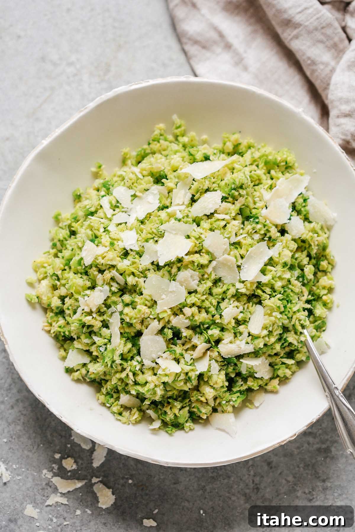 Crispy Parmesan Brussels Sprouts Salad 4 close up of a Parmesan Brussels Sprouts Salad with a spoon and shaved parmesan on top, highlighting its fresh appeal.