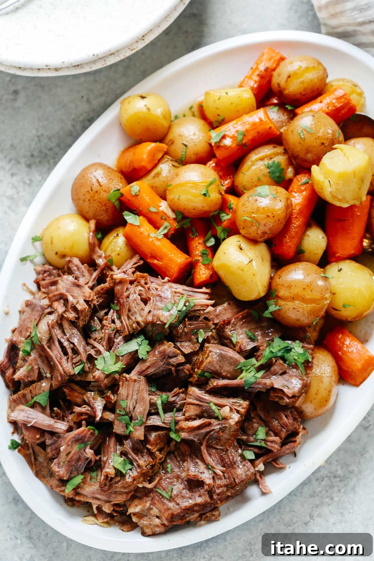 Pressure cooker pot roast recipe in a white serving plate with carrots and potatoes.