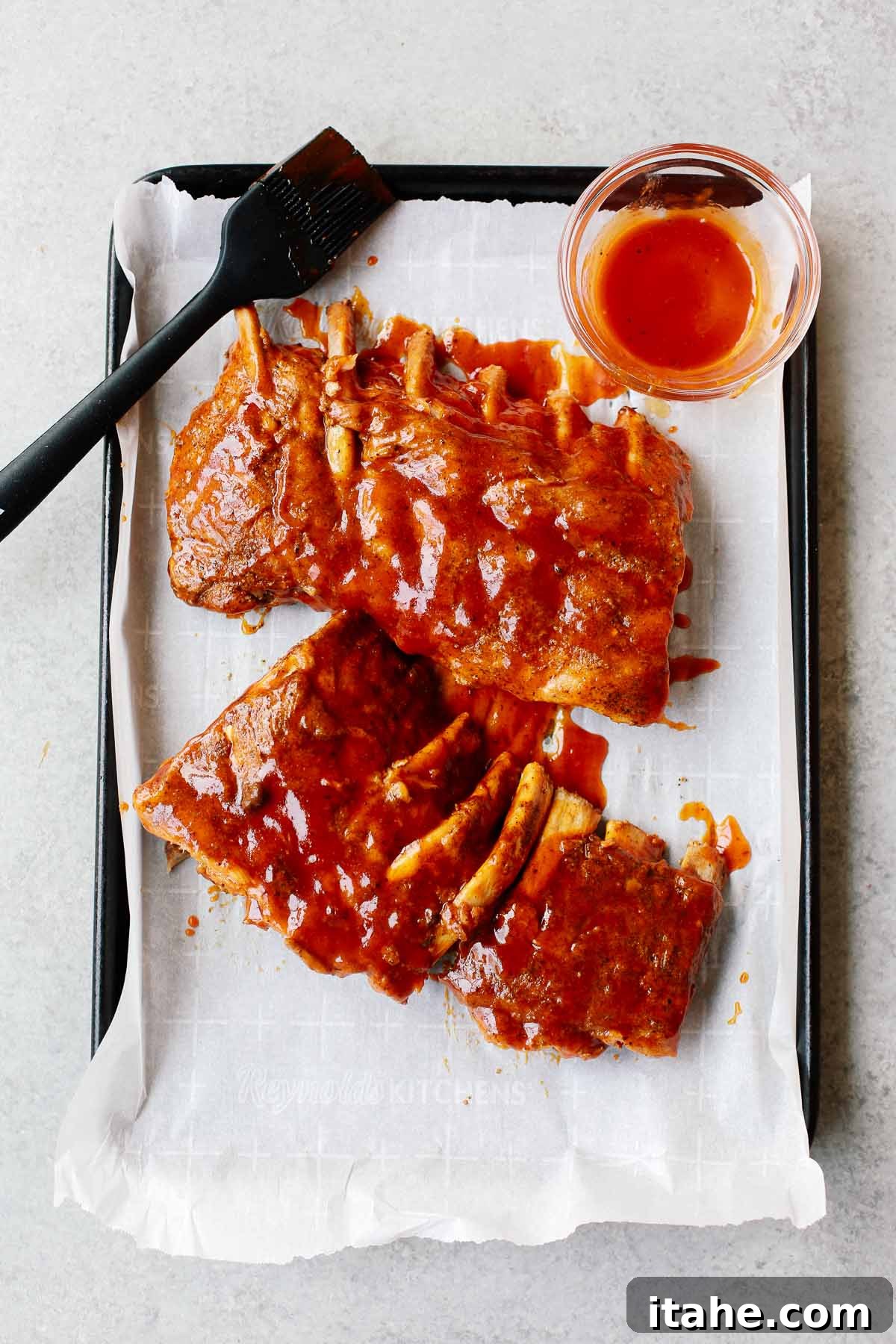 cooked ribs on a sheet pan with bbq sauce brushed on