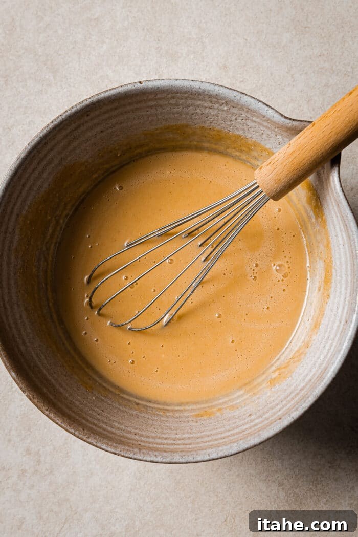 Creamy Peanut Butter Flapjacks 5 A large bowl of wet pancake batter ingredients with a whisk in it.