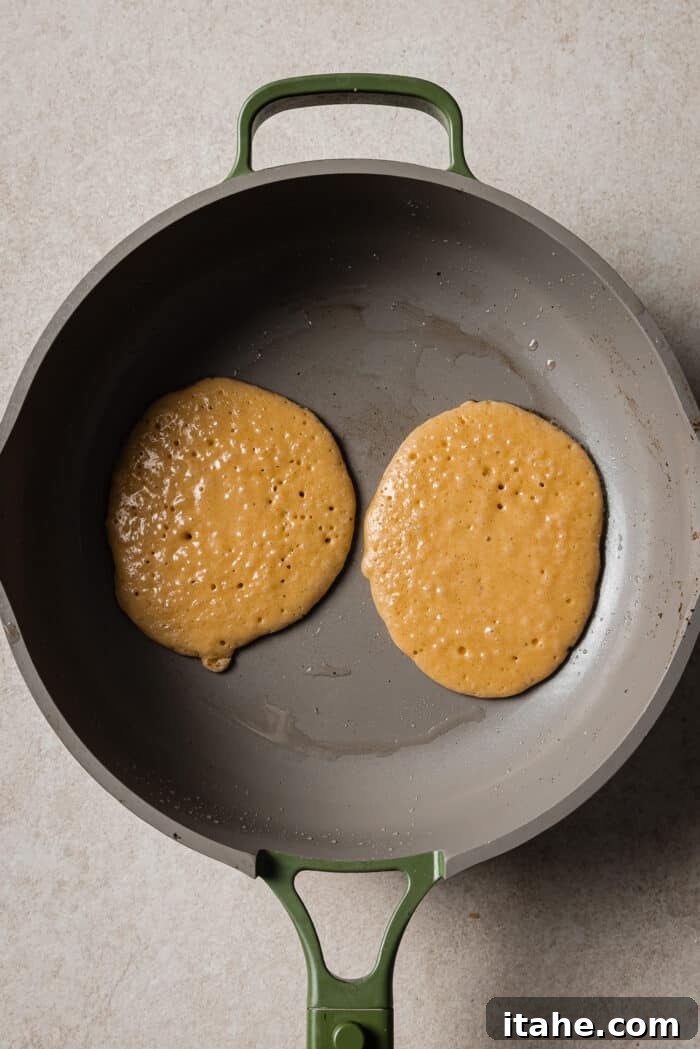 Creamy Peanut Butter Flapjacks 8 Two uncooked peanut butter pancakes cooking in a skillet.