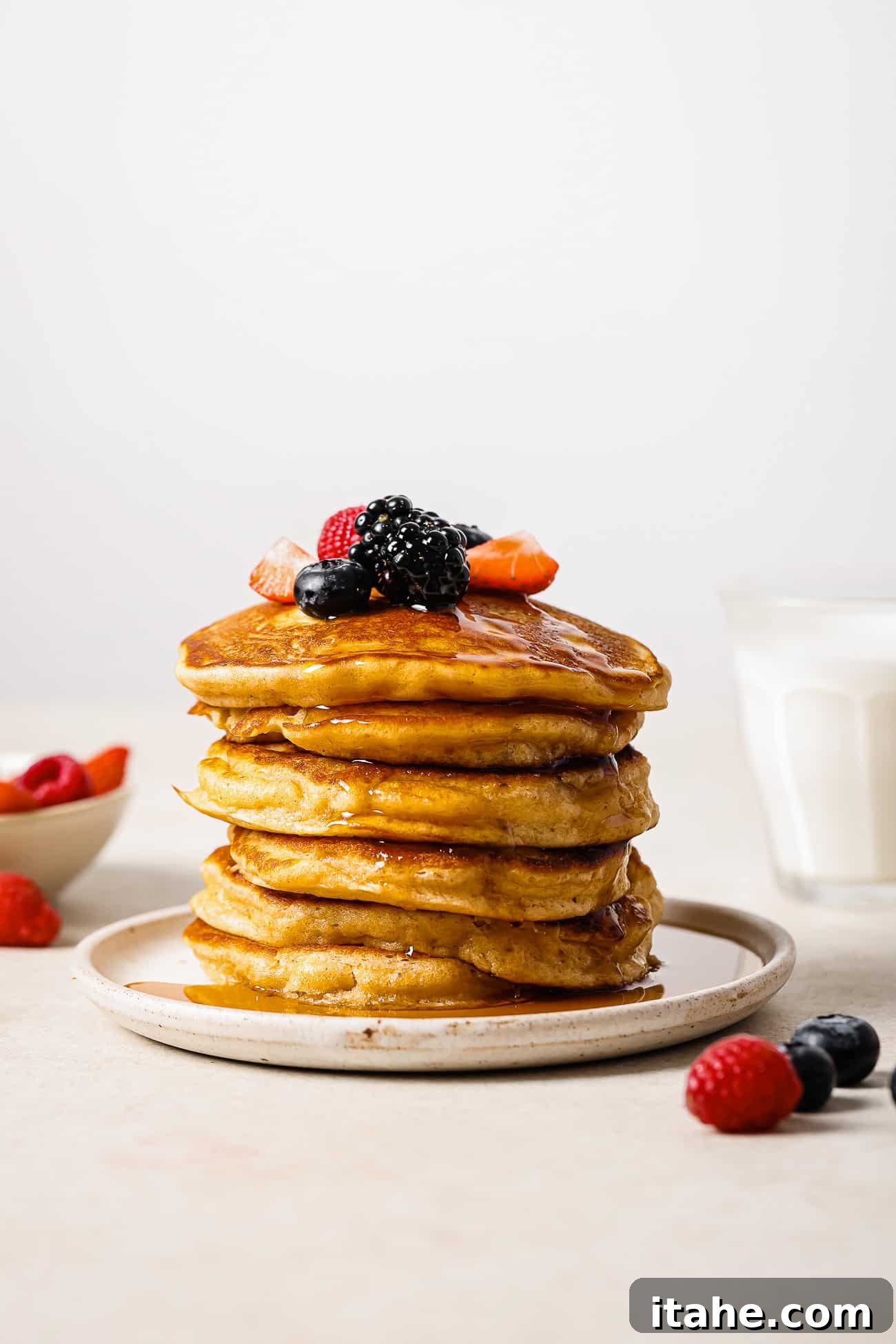 Creamy Peanut Butter Flapjacks 10 A stack of peanut butter pancakes topped with syrup and berries on a white plate.