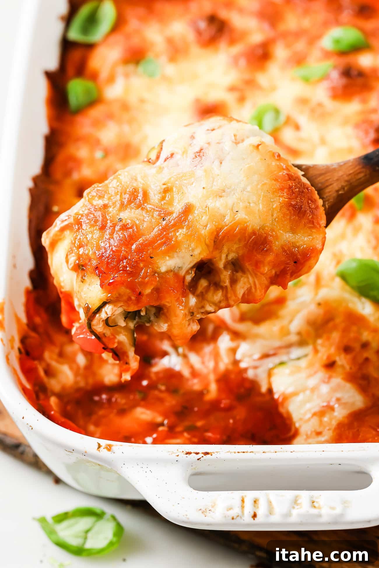 A serving of zucchini lasagna rolls being spooned out of a casserole dish, showing the cheesy layers.