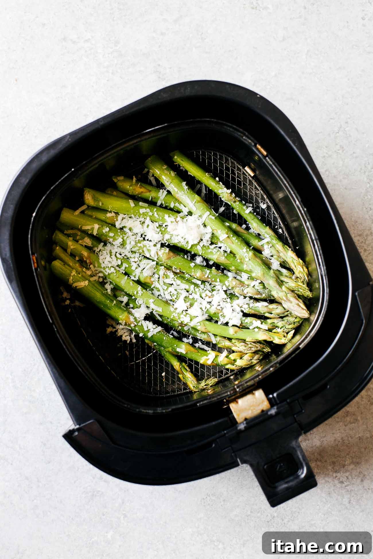 Overhead view of seasoned asparagus cooking inside an air fryer