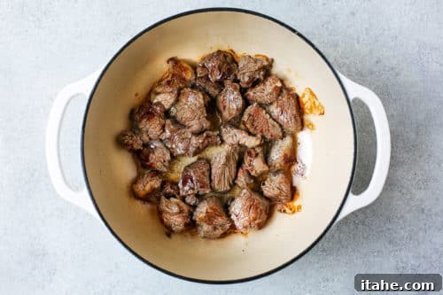 Seared beef chuck cubes cooking in a Dutch oven pot, developing a rich brown crust.