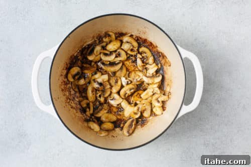Sautéed mushrooms cooking in a Dutch oven pot, turning golden brown.