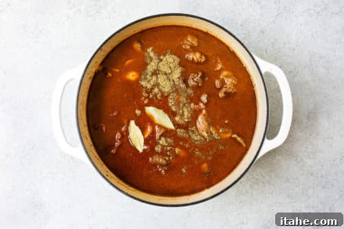 Beef stew simmering in a Dutch oven pot with all liquids and herbs, ready for braising in the oven.