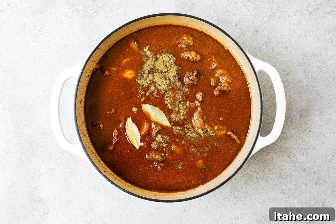 Hearty beef stew simmering with liquids and aromatics inside a Dutch oven pot, ready for braising.