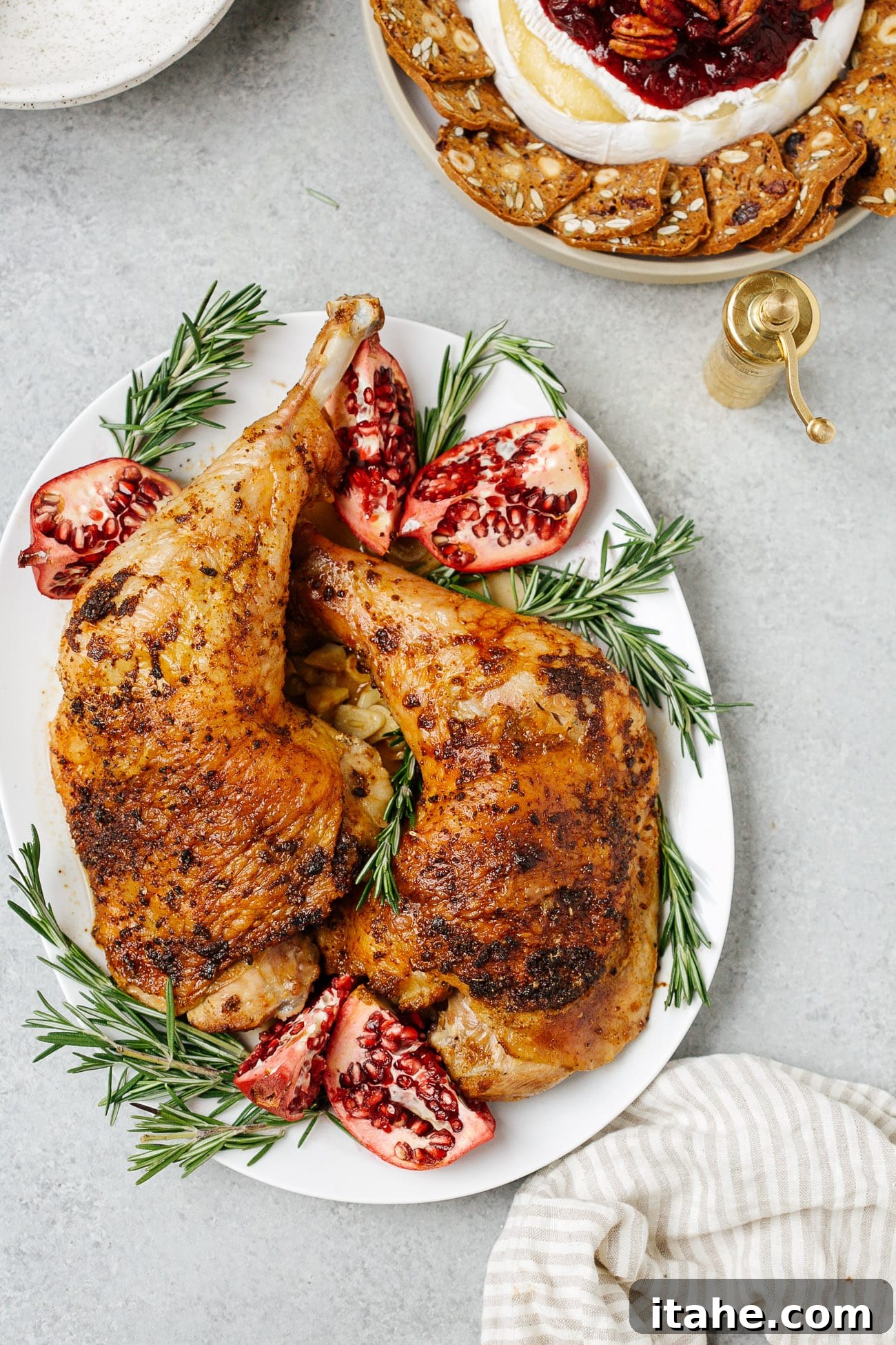 Overhead view of a platter with two turkey legs with rosemary and pomegranate as garnish. 