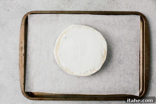 Brie cheese on a parchment-lined baking sheet, ready to be baked.