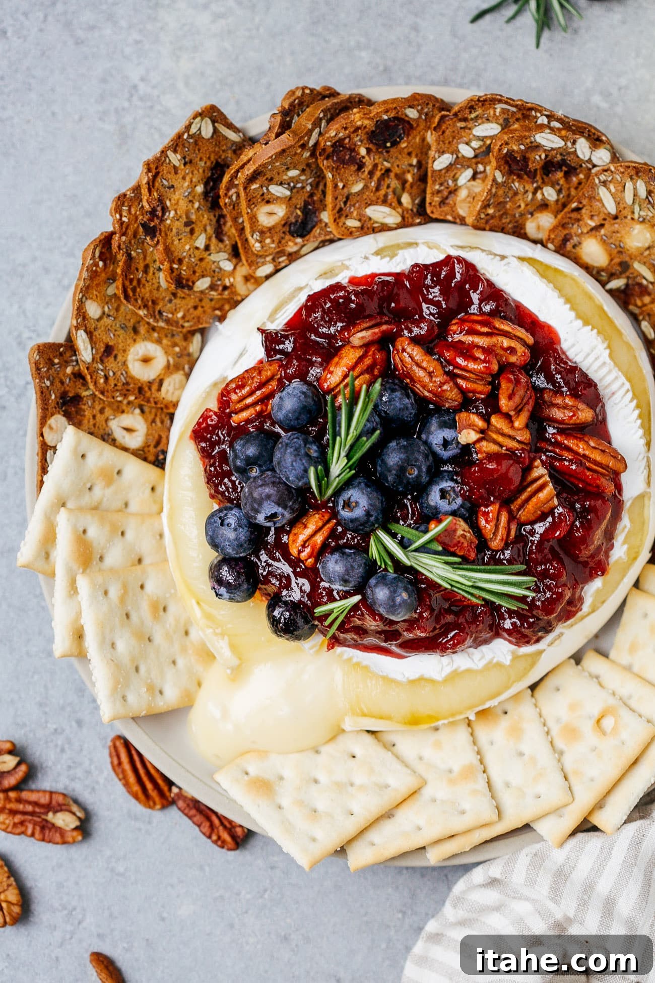 Warm Cranberry Brie Delight 3 Overhead view of a baked brie with cranberry sauce served with crackers and fresh rosemary.