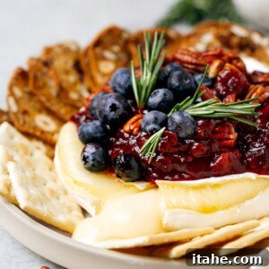 Baked Brie with Cranberry Sauce, topped with cranberries, pecans, and rosemary.