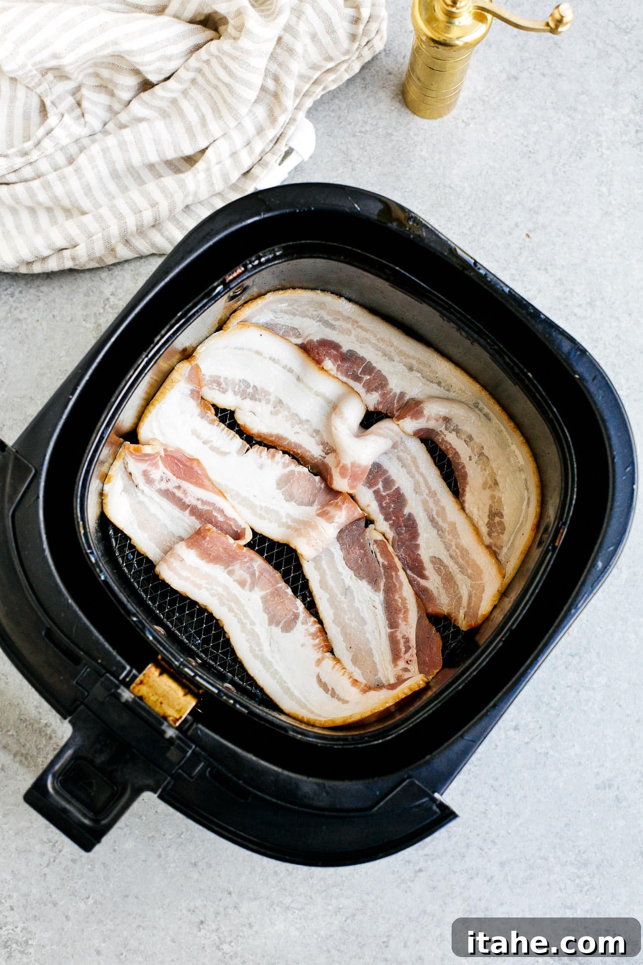 overhead view of raw bacon inside of a air fryer basket 