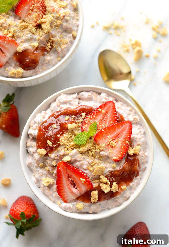 A tempting bowl of strawberry cheesecake overnight oats, generously topped with strawberry jam, fresh sliced strawberries, and crushed graham crackers.