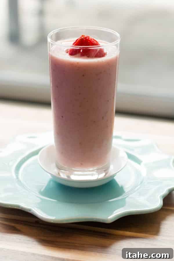 A tall glass filled with a vibrant strawberry and papaya smoothie, garnished with fresh strawberry slices.