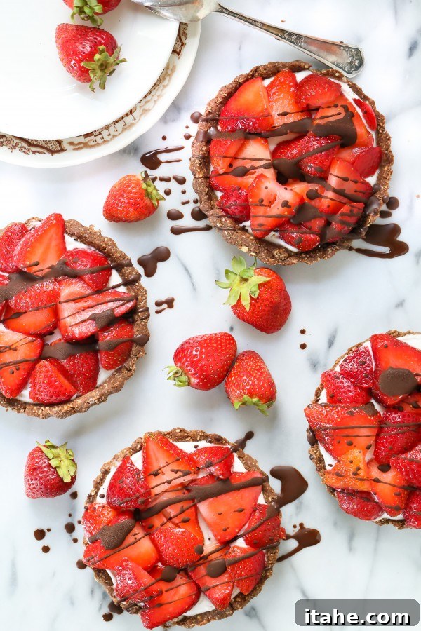 Four charming no-bake mini strawberry pies, elegantly drizzled with chocolate, on a serving plate.