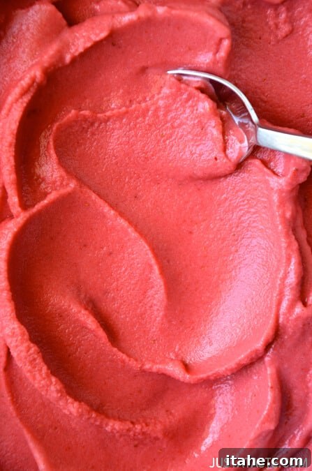 A close-up view of luscious strawberry frozen yogurt, with a silver spoon poised within the creamy treat.