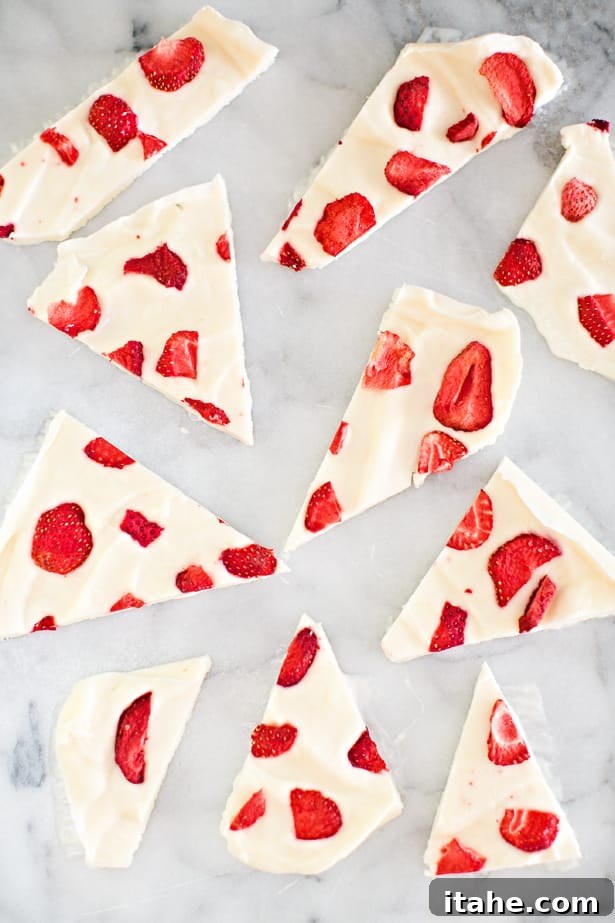 Irregular pieces of white frozen yogurt bark speckled with vibrant red strawberry fragments.