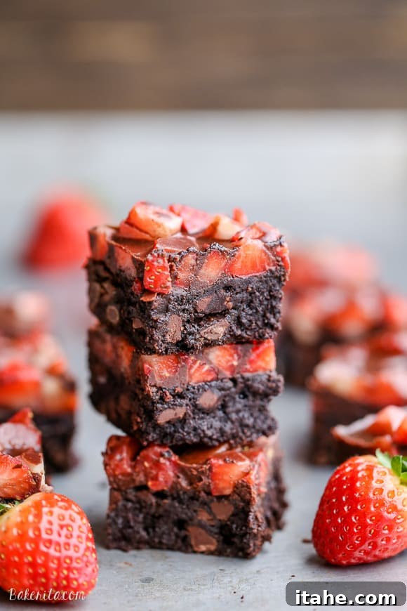 A delectable stack of three chocolate-covered strawberry brownies, artfully arranged next to whole fresh strawberries.