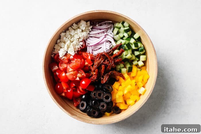 Freshly chopped ingredients for Mediterranean Salad, including tomatoes, cucumbers, bell peppers, and onions, neatly arranged in separate piles.