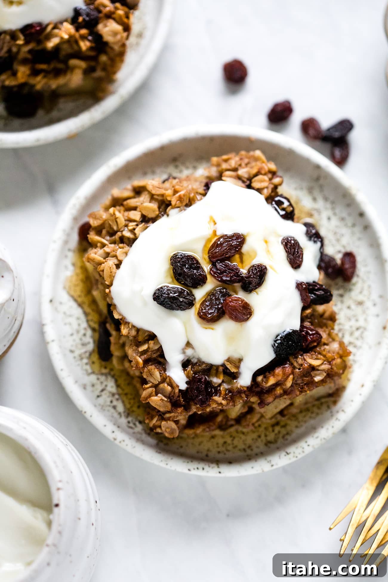 Spiced Apple Raisin Baked Oatmeal 10 A perfectly portioned slice of baked oatmeal with apples and raisins, adorned with a swirl of Greek yogurt, ready to be enjoyed.