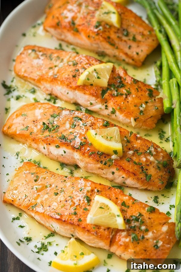 Four pieces of beautifully pan-seared salmon on a baking sheet, gleaming with garlic lemon butter sauce.