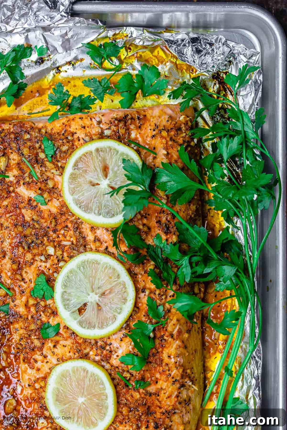 An overhead view of a perfectly baked salmon fillet adorned with lemon and garlic on a baking sheet.