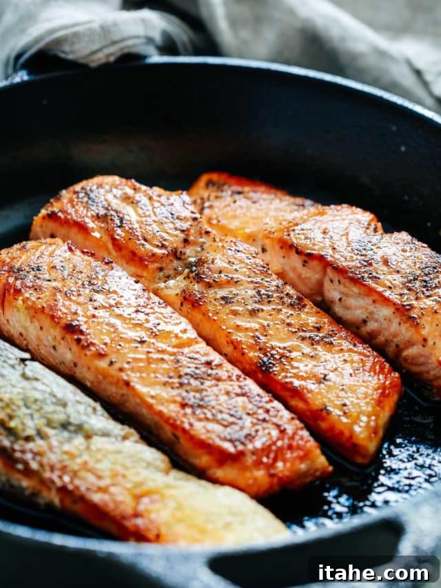 Close-up of four perfectly pan-seared salmon fillets in a cast-iron skillet, skin deliciously crispy.