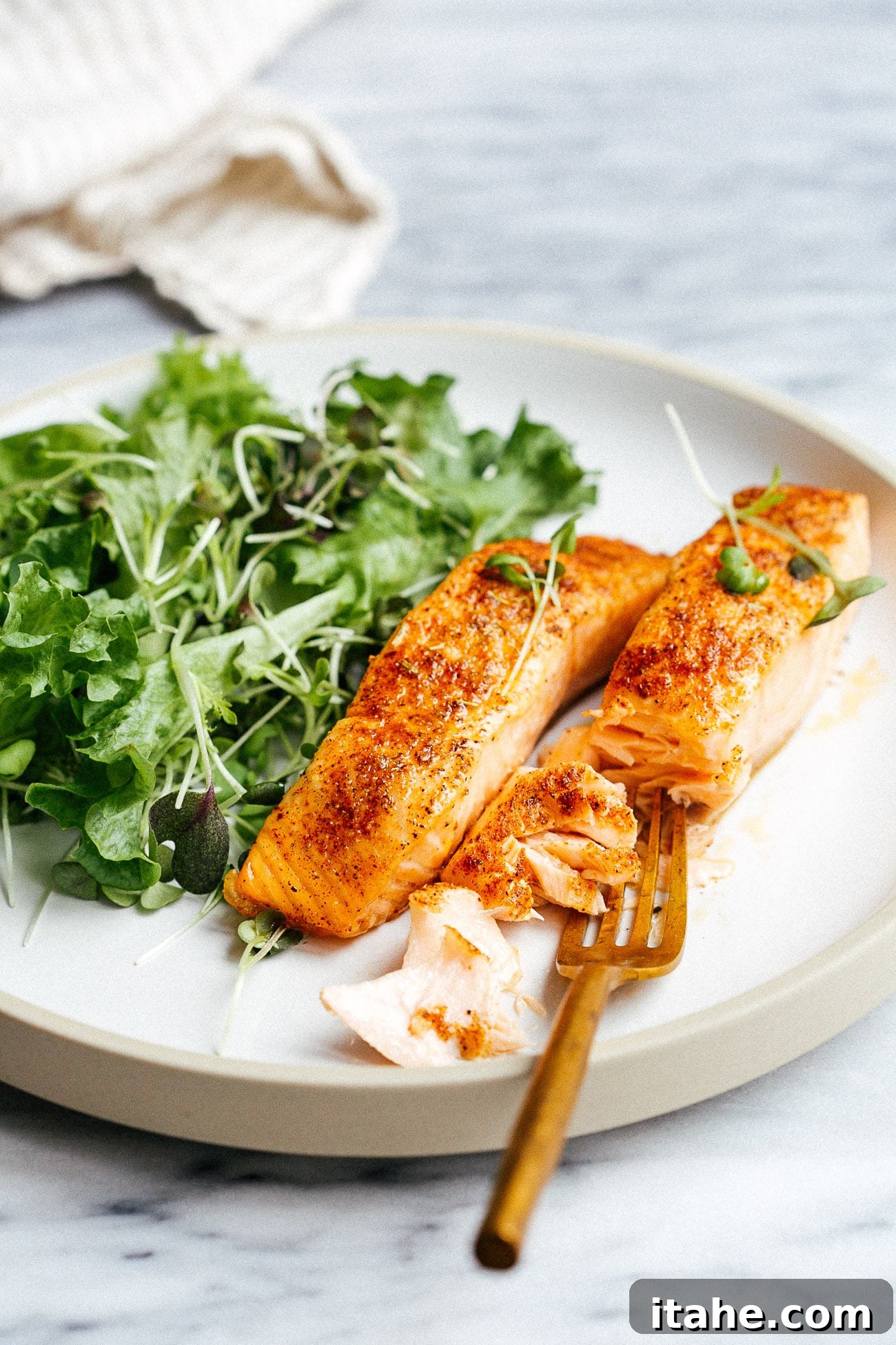 A close-up of a white plate featuring succulent air fryer salmon alongside a fresh green salad.