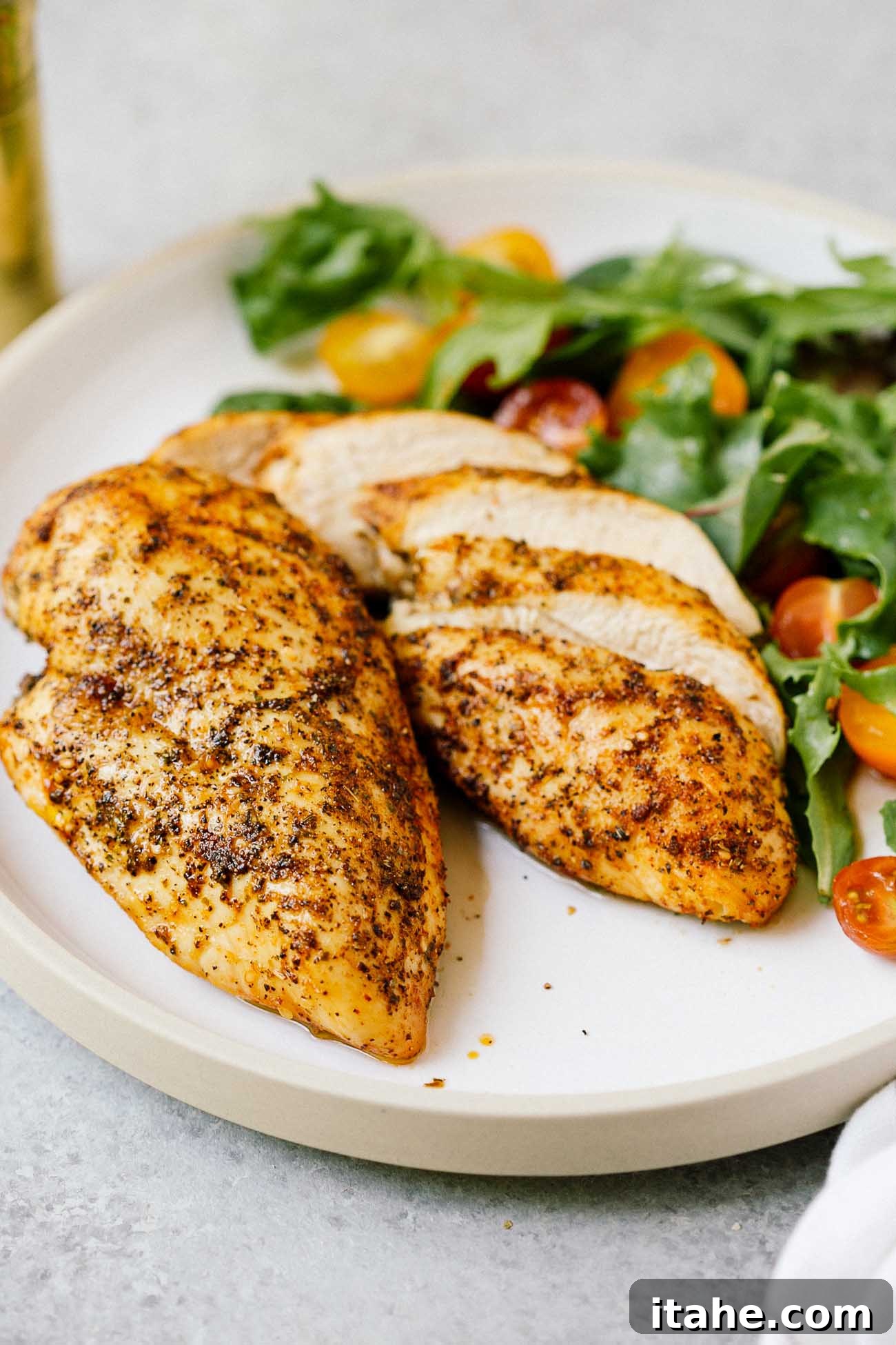 Closeup of two perfectly golden-brown air fryer chicken breasts on a white plate, ready to be served.