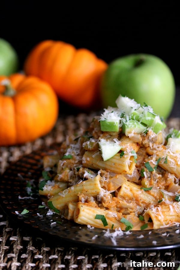 The Ultimate Fall Pumpkin Sauces 7 Rigatoni pasta beautifully coated in a rich pumpkin sauce, mixed with savory sausage and crisp green apple slices, served on an elegant black plate.