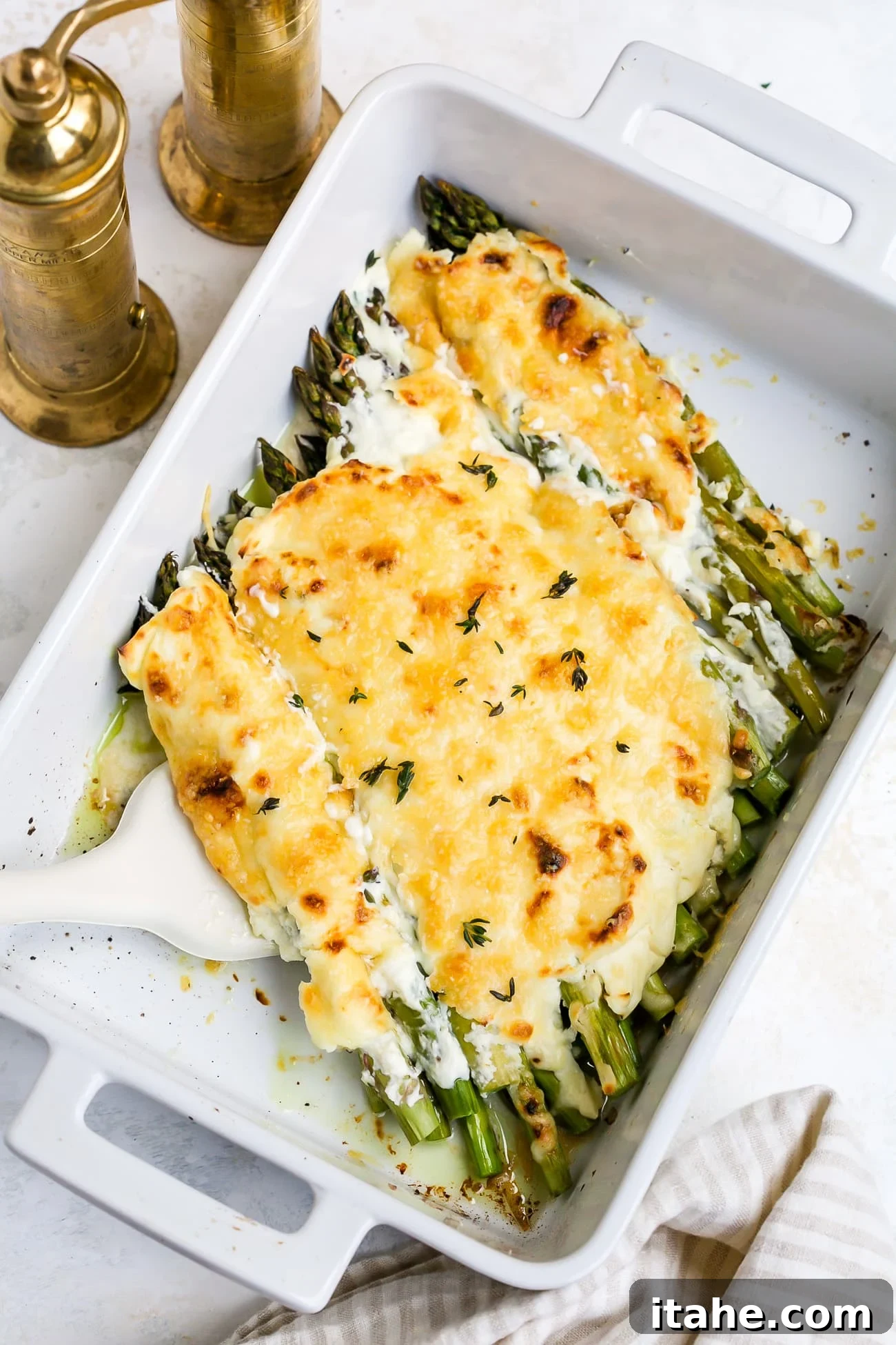 A golden-brown cheesy asparagus casserole in a white baking dish, freshly baked and ready to serve.