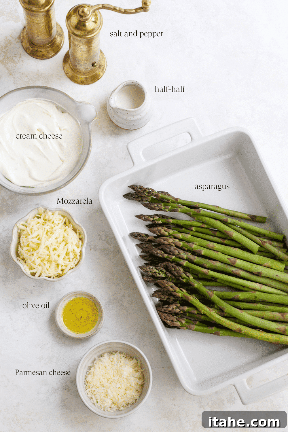 Arrangement of fresh asparagus, olive oil, cream cheese, half and half, mozzarella, parmesan, and parsley on a kitchen counter.
