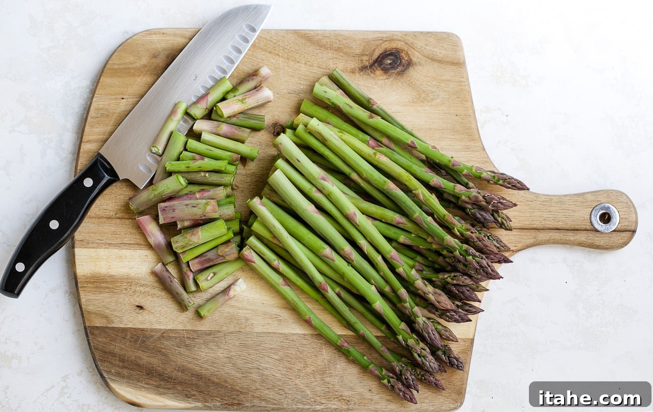 A person's hands cutting woody ends from asparagus stalks on a wooden cutting board.