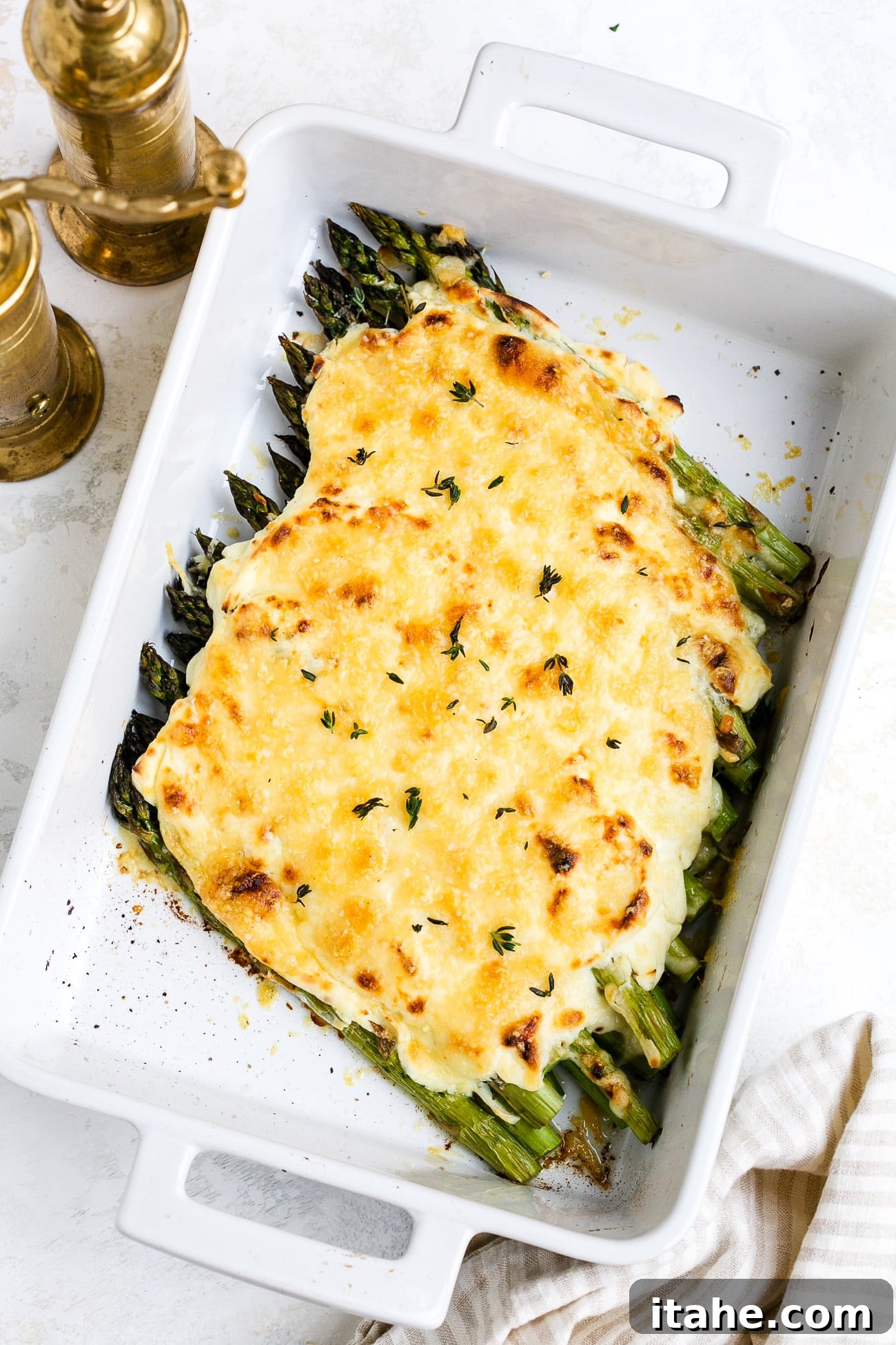 A close-up of the freshly garnished cheesy asparagus casserole in a white baking dish, ready to be served.
