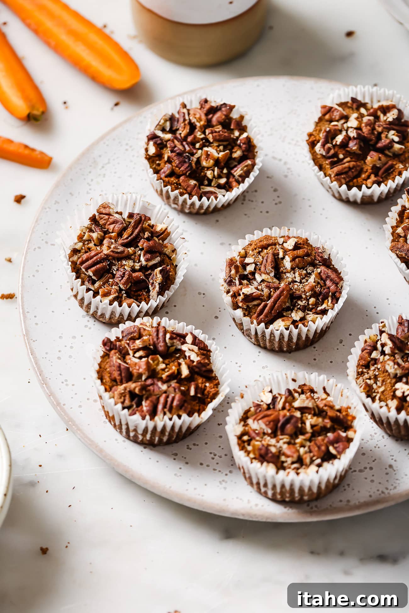 Spiced Gluten-Free Carrot Muffins 2 Gluten-free carrot muffins on a white serving dish.