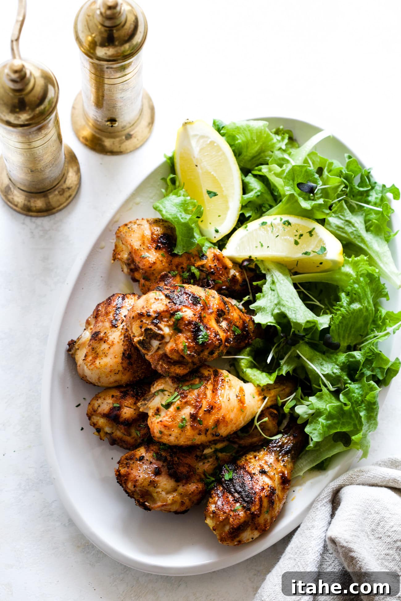 Perfectly Charred Chicken Legs 2 Perfectly grilled chicken legs served on a white plate with fresh green lettuce and bright lemon slices, showcasing a golden-brown, crispy skin and juicy interior.