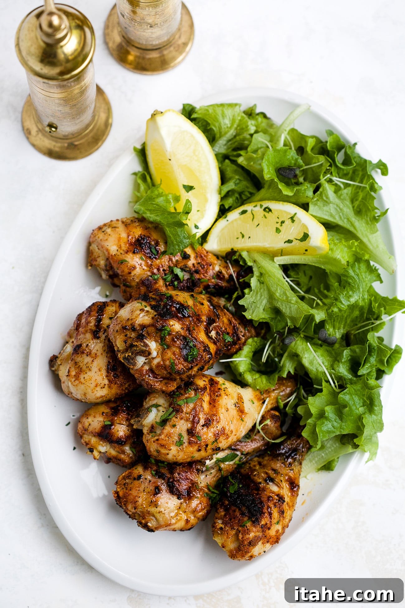 Perfectly Charred Chicken Legs 5 A perfectly grilled chicken leg, golden brown with crispy skin, presented elegantly on a white plate alongside fresh green lettuce and bright lemon slices, ready to be enjoyed as a main dish.