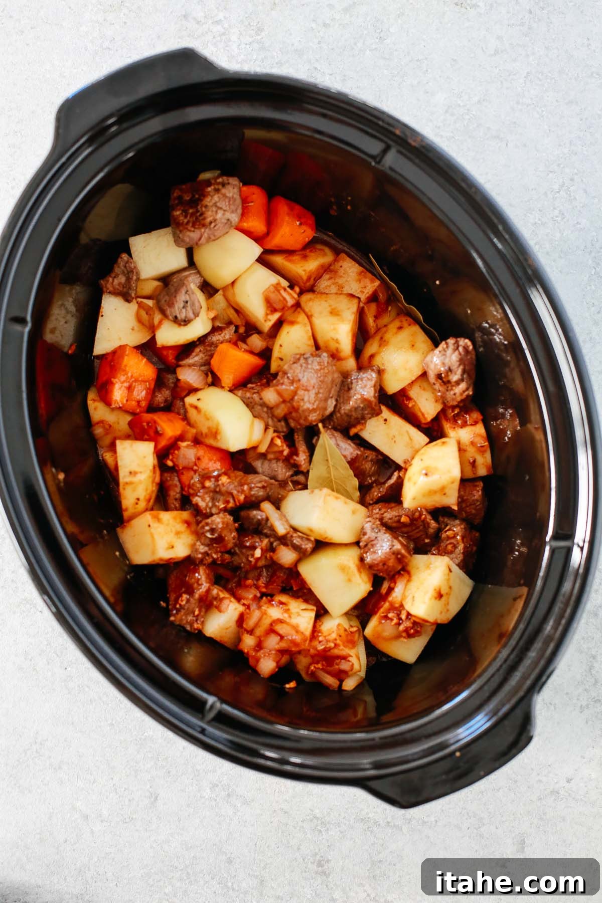 Nourishing Slow Cooker Beef Stew 4 Overhead image of ingredients for the beef stew being added to the slow cooker before cooking.