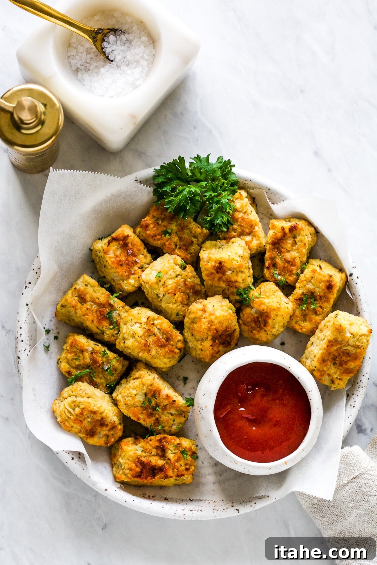 Crispy Cauliflower Bites 2 Crispy, cheesy cauliflower tots served in a white dish with a side of ketchup, ready to be enjoyed.