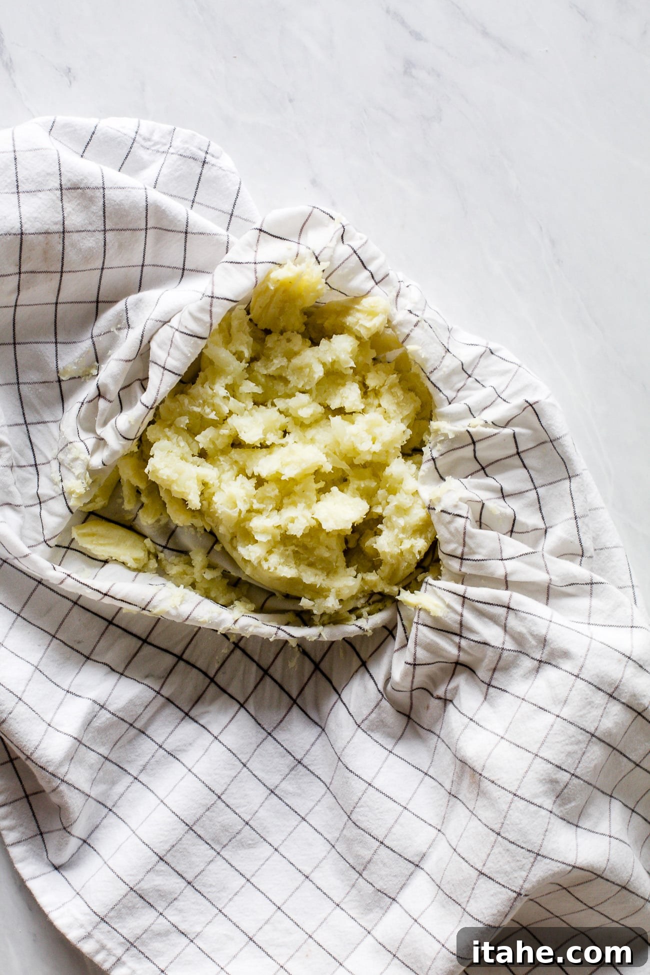 Crispy Cauliflower Bites 6 Close-up of hands vigorously squeezing excess liquid from pureed cauliflower using a clean kitchen towel, a critical step for achieving crispy cauliflower tots.