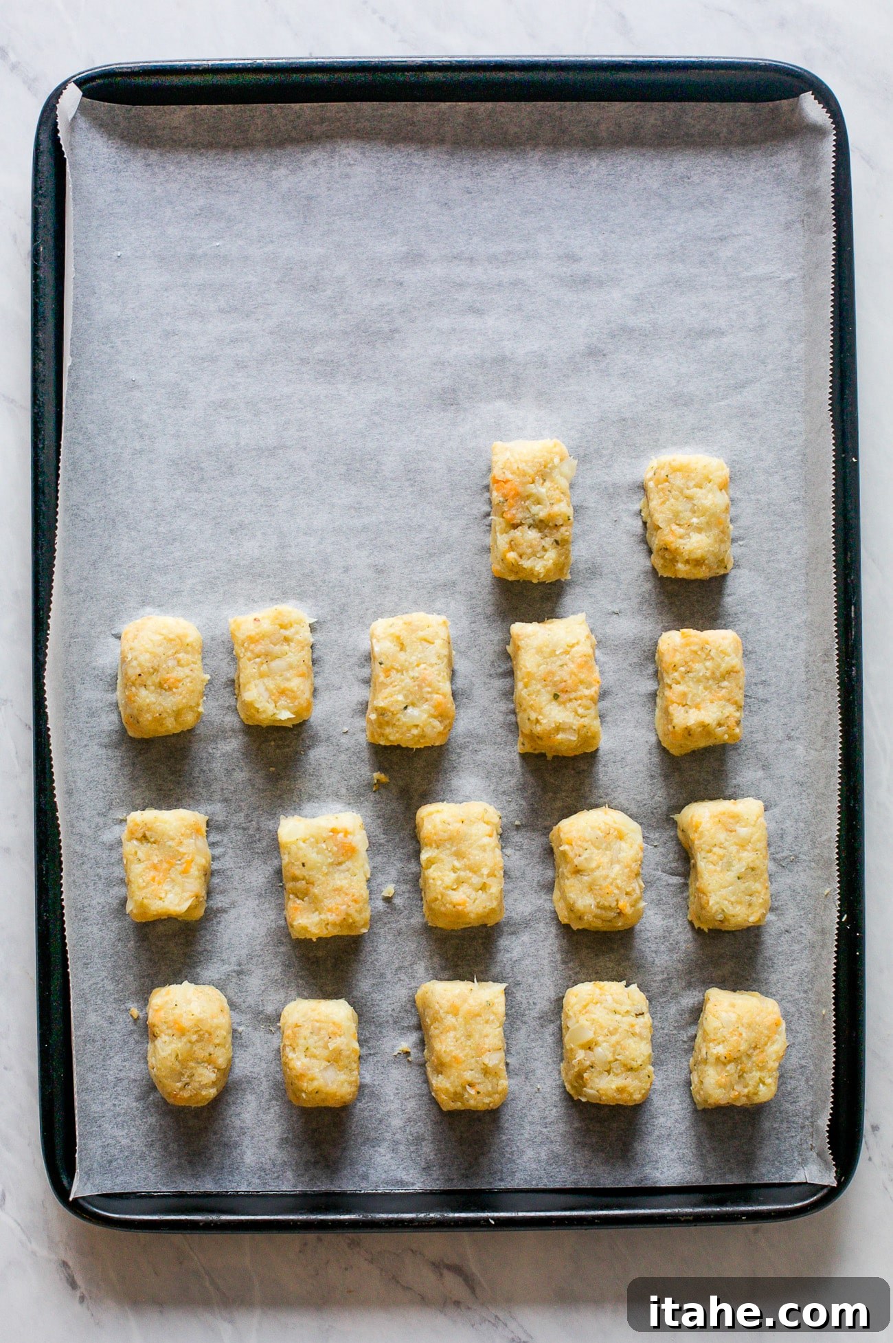 Crispy Cauliflower Bites 8 Unbaked cauliflower tots neatly arranged and spaced on a parchment paper-lined baking sheet, patiently awaiting the oven.