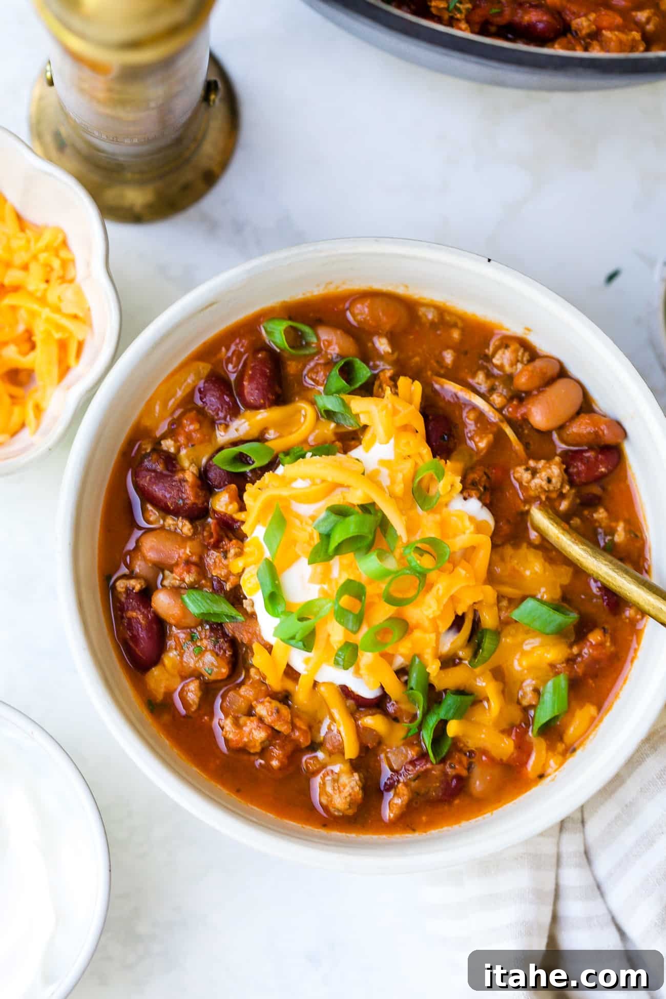 overhead view of a white bowl with classic chili recipe, garnished with cheese, sour cream, and green onions