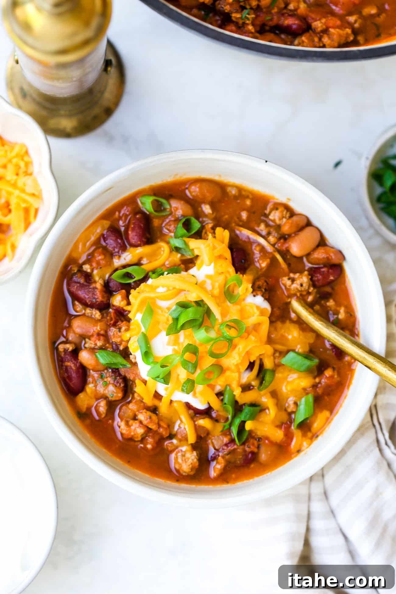 Close up of a white bowl filled with classic chili, generously topped with shredded cheese, sour cream, and green onions.