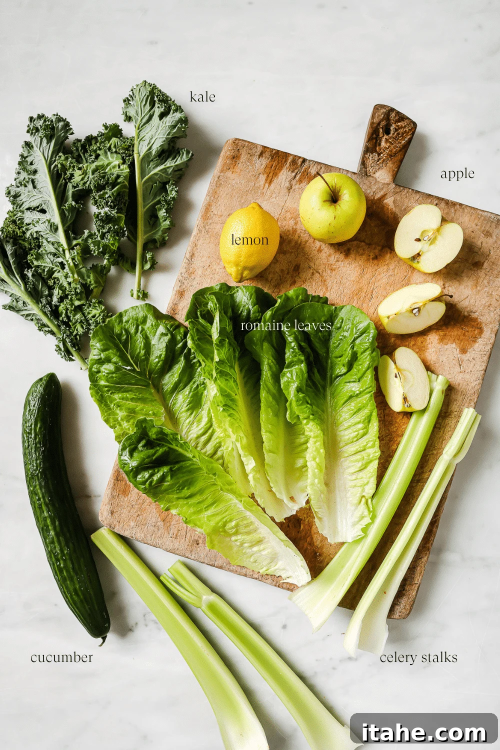 Fresh ingredients for green juice, including green apples, celery, cucumber, kale, romaine, and lemons, neatly arranged on a wooden cutting board, ready for preparation.