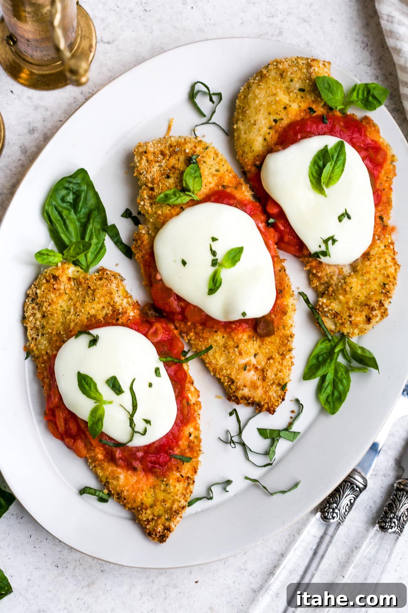 Crispy Baked Chicken Parmesan 2 Perfectly baked chicken parmesan, garnished with fresh basil, served on a pristine white plate.