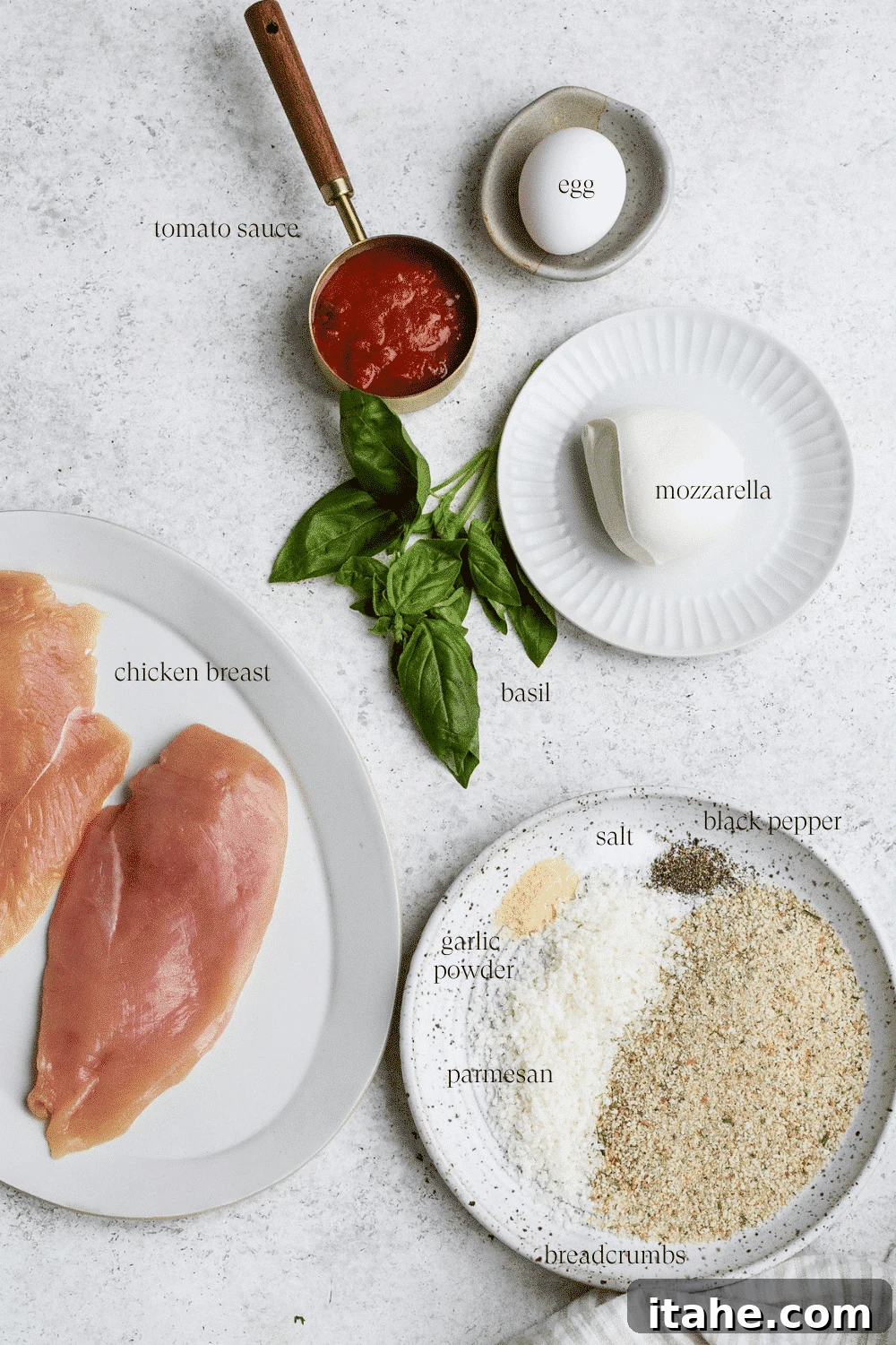 Crispy Baked Chicken Parmesan 3 Fresh ingredients laid out for making healthy baked chicken parmesan, including chicken breasts, fresh mozzarella, breadcrumbs, tomato sauce, basil, and Parmesan.