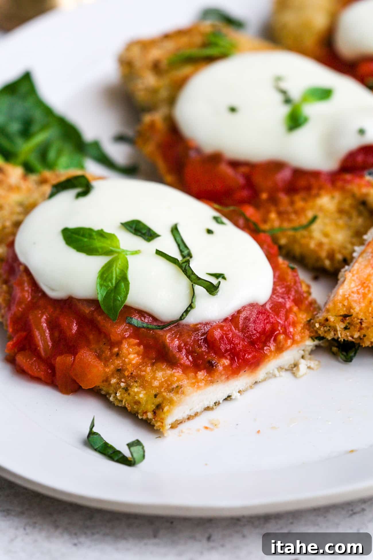 Crispy Baked Chicken Parmesan 7 A beautifully arranged serving of baked chicken parmesan with melted cheese and fresh basil on a white plate, ready to be enjoyed.